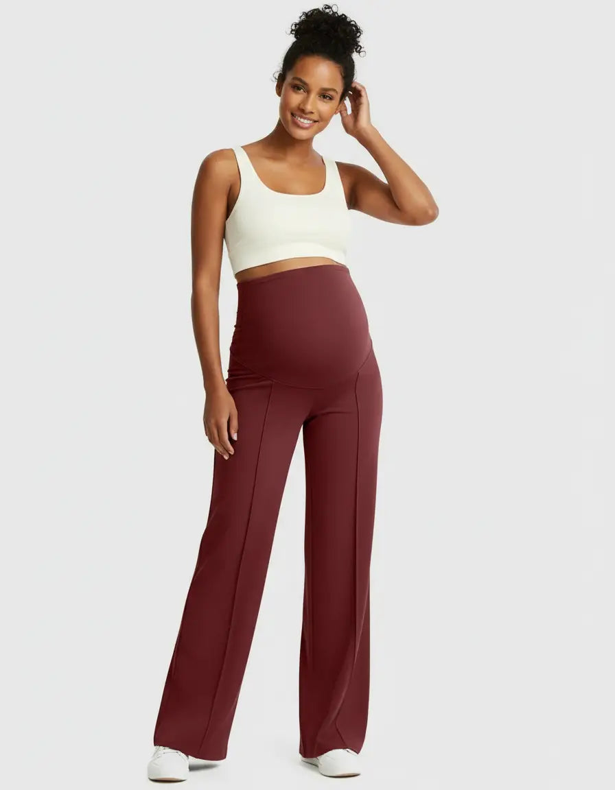Smiling woman in high-waist, relaxed-fit burgundy maternity pants with a cream crop top.