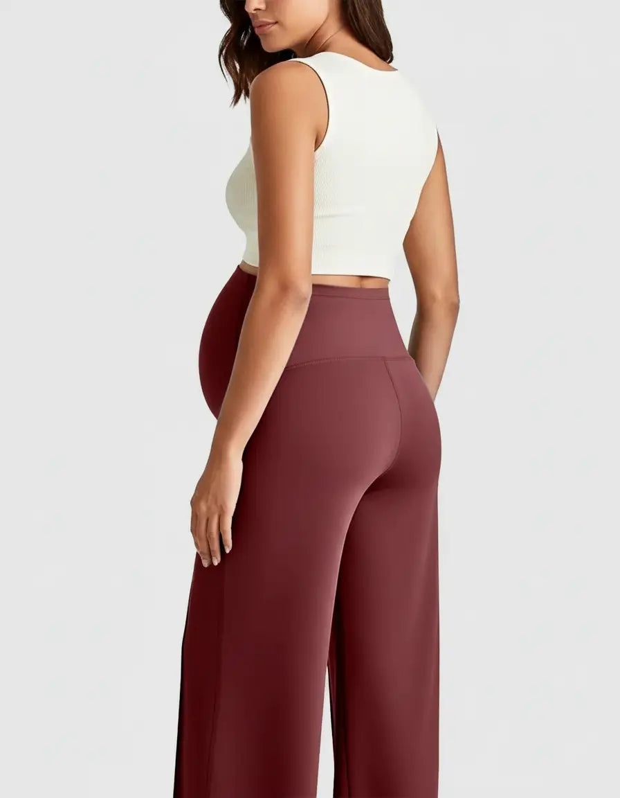 Pregnant woman in high-waist, relaxed-fit burgundy maternity pants and a white crop top, viewed from behind.