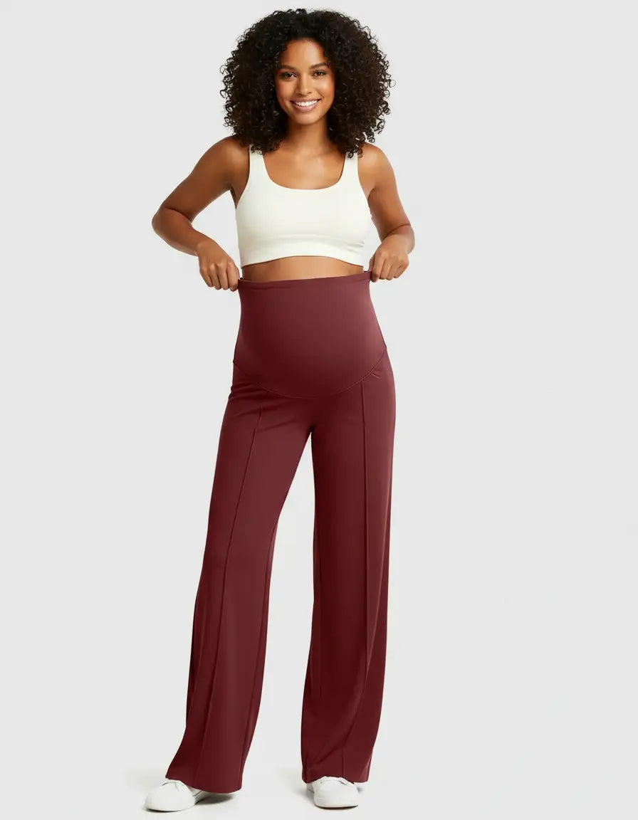 Smiling woman in white crop top and high-waisted, relaxed-fit burgundy maternity pants.