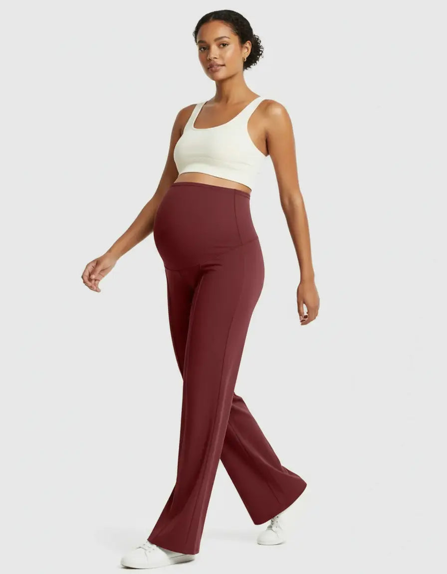 Woman in high-waist, relaxed-fit burgundy maternity pants and a white crop top, walking.