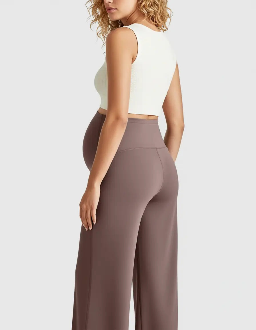 Pregnant woman from behind wearing high-waist, relaxed-fit brown maternity pants and a white crop top.