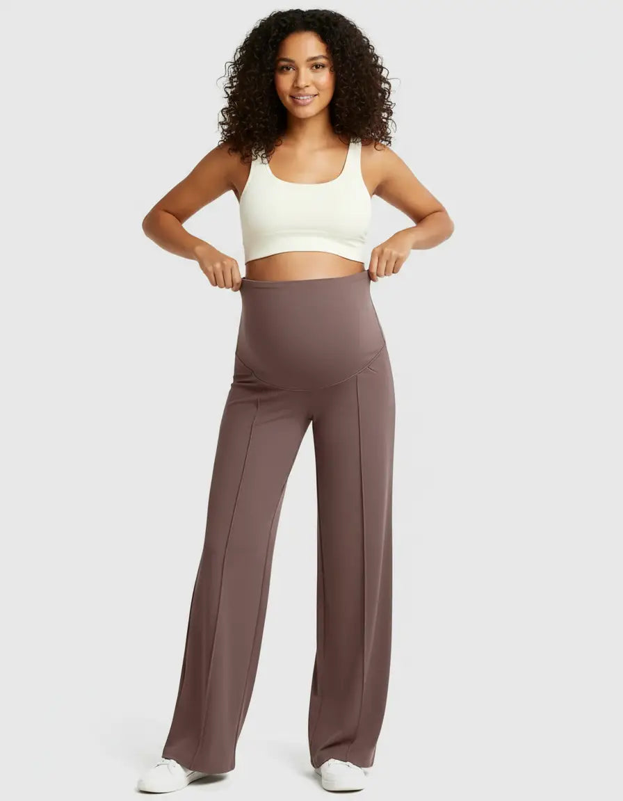 Smiling pregnant woman in a white crop top and high-waisted, relaxed-fit brown maternity pants.