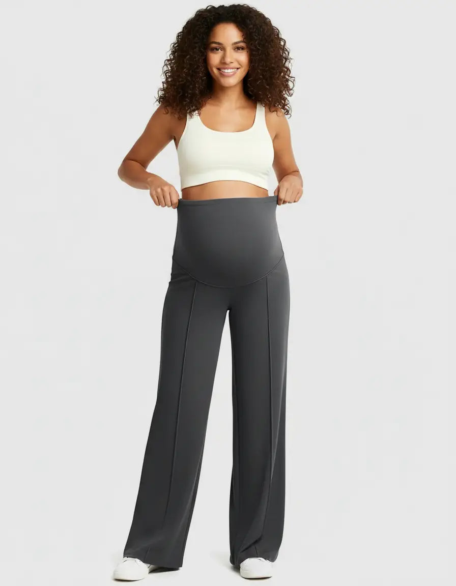 Smiling woman in dark gray high-waist maternity pants with a relaxed fit and a white crop top.