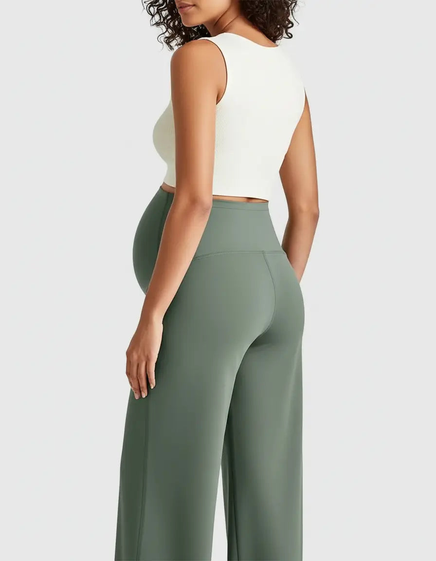 Pregnant woman from behind wearing high-waist, relaxed-fit sage green maternity pants and a white crop top.