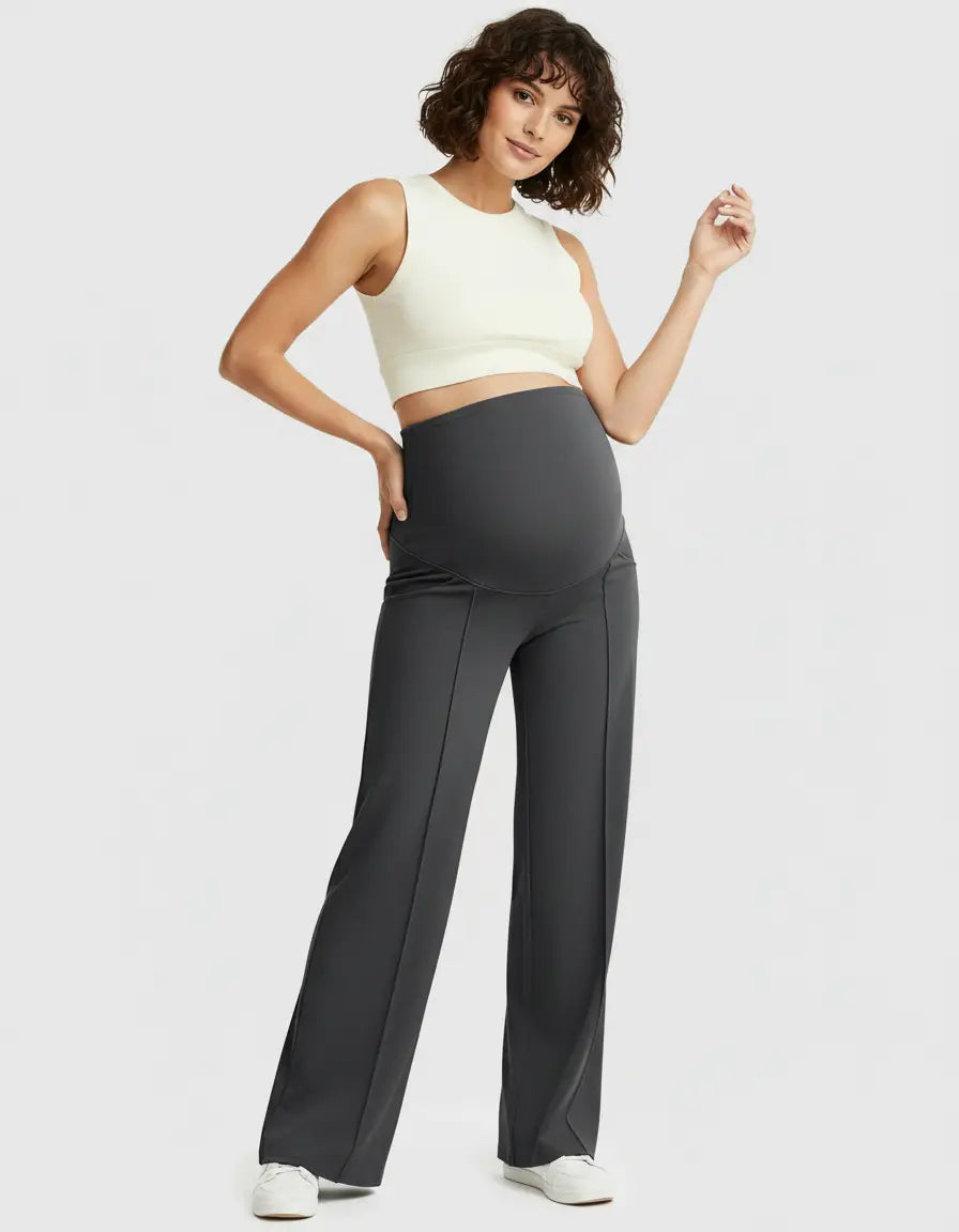 Woman models dark gray high-waist maternity pants with a relaxed fit and a white crop top.
