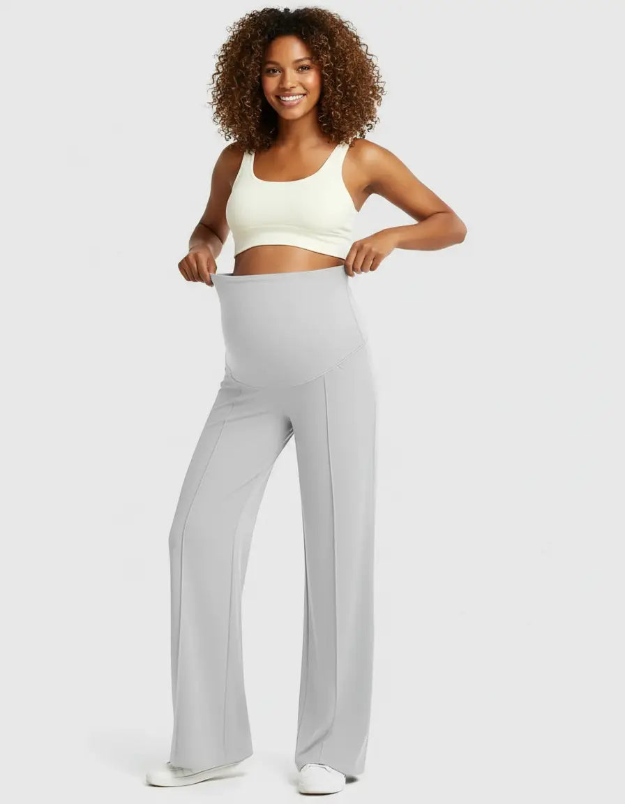 Smiling woman in light gray high-waist maternity pants with a relaxed fit and a cream sports bra.