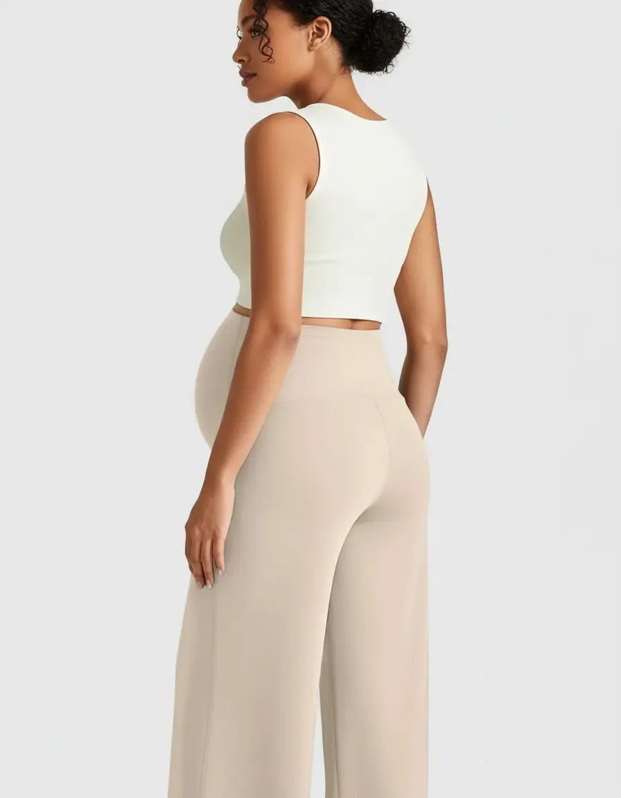 Maternity model in beige high-waist relaxed-fit pants and a white crop top, showcasing comfort.