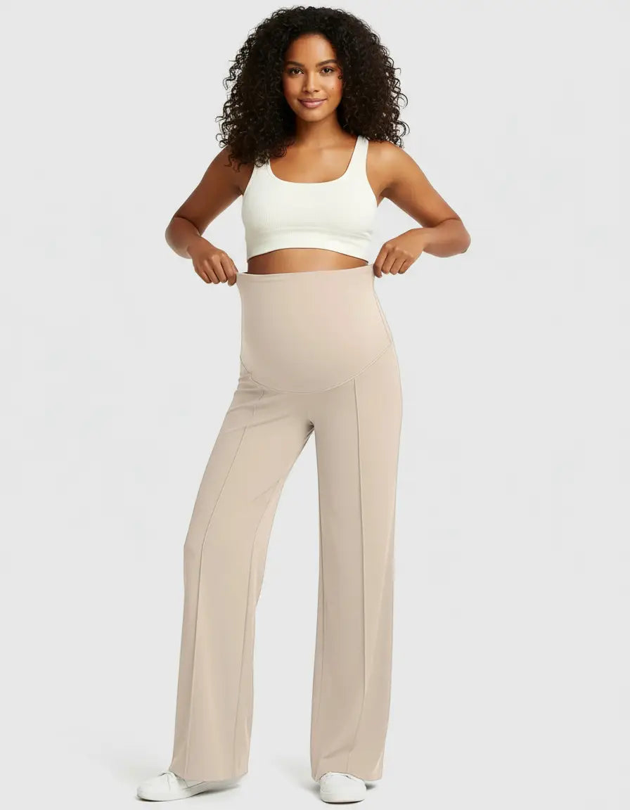 Smiling pregnant woman in a white crop top and beige high-waist maternity pants with a relaxed fit.