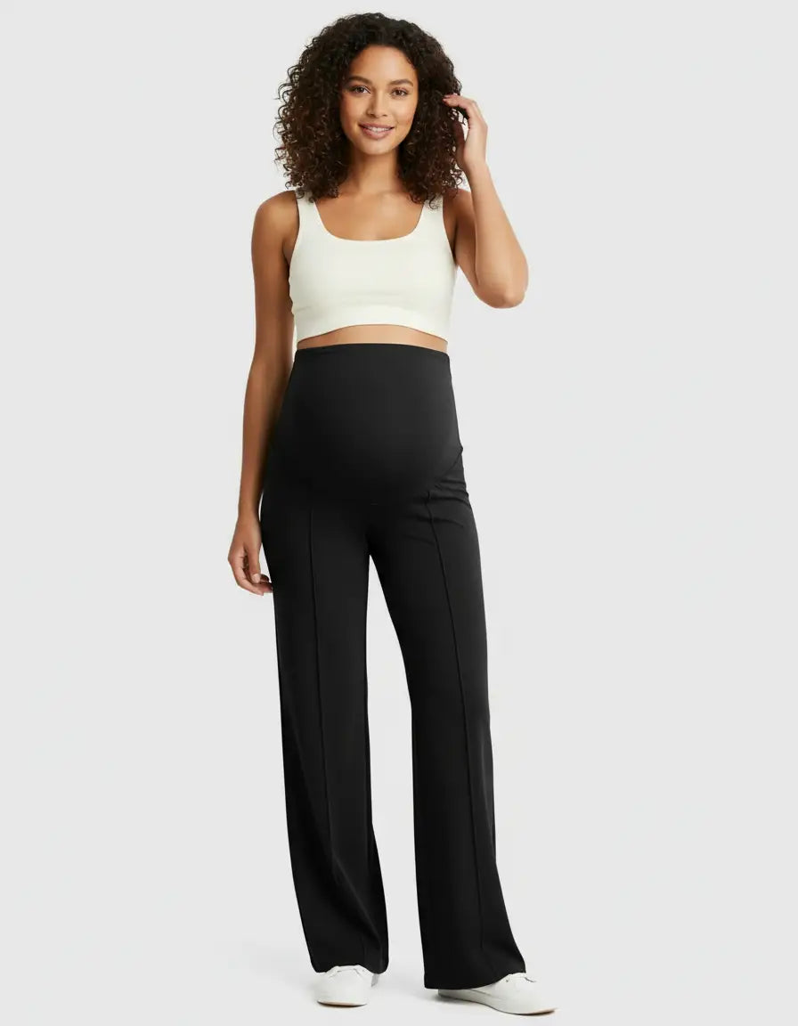 Smiling pregnant woman in black high-waist maternity pants with a relaxed fit and a white crop top.