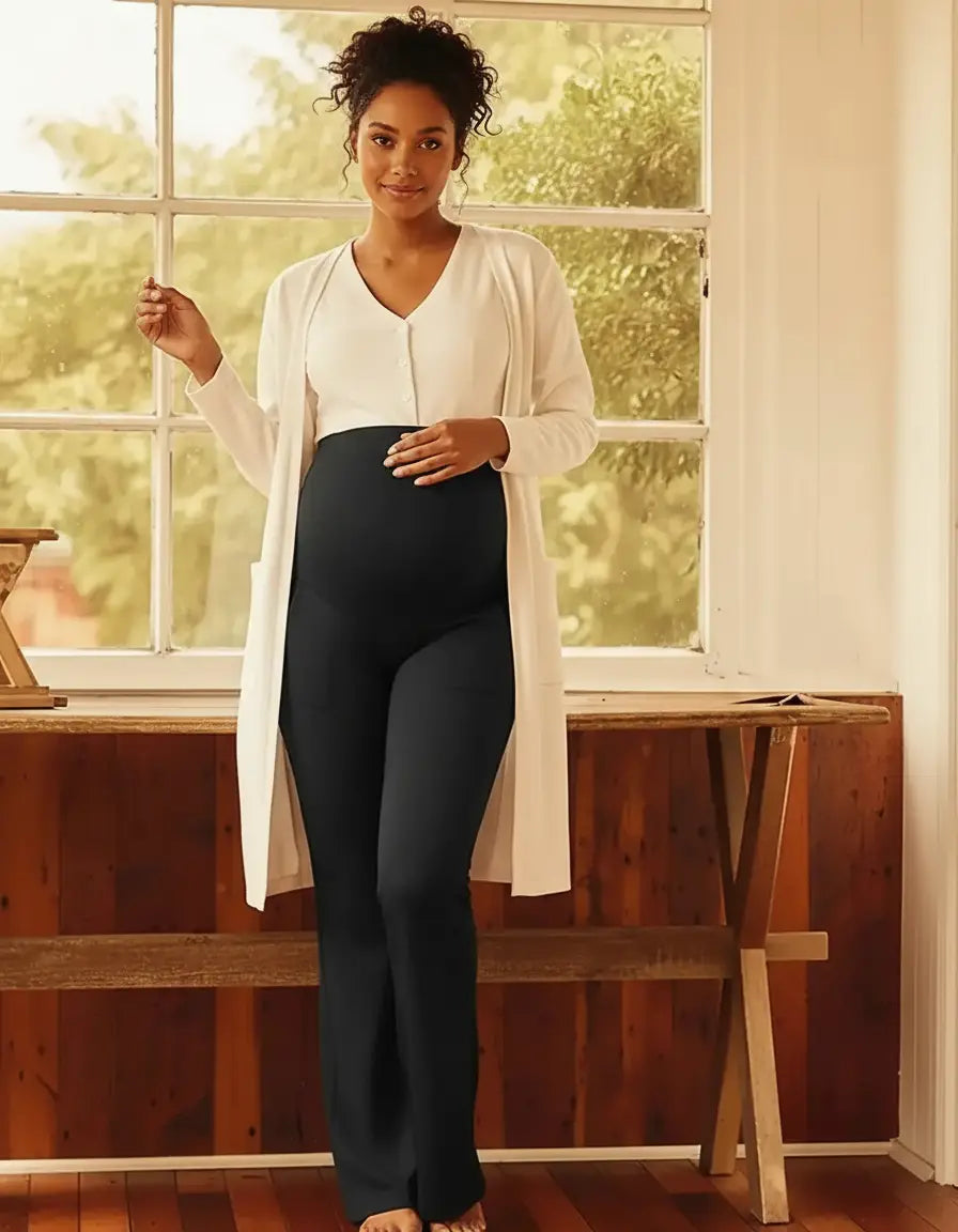 Pregnant woman in black high-waist pocketed flare-leg maternity leggings and a white cardigan.