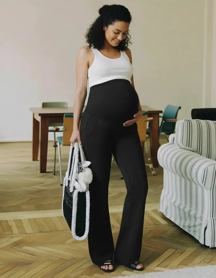 Smiling pregnant woman in black high-waist flare-leg maternity leggings and white tank top.
