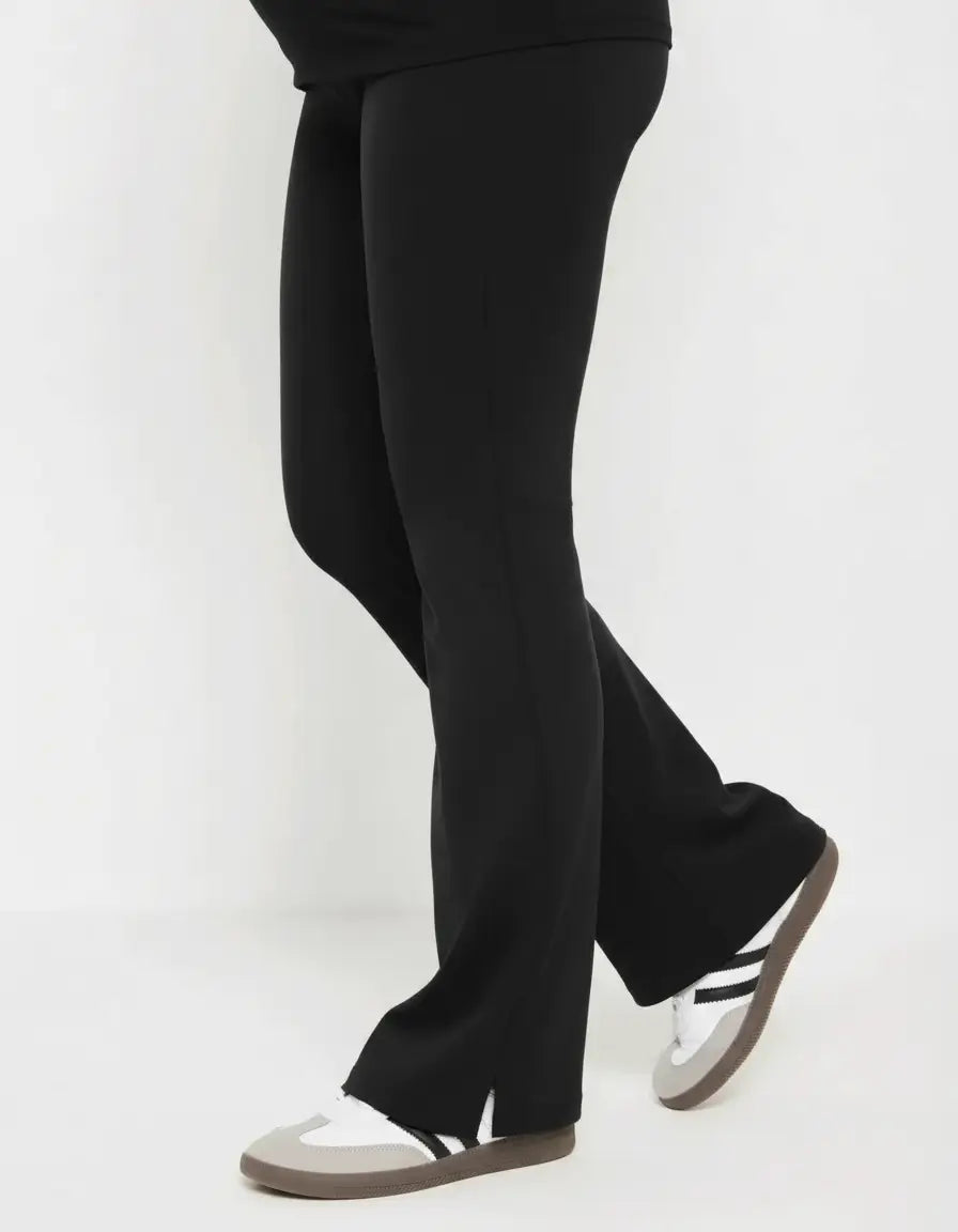 Black high-waist flare-leg maternity leggings with side slits, paired with sneakers.