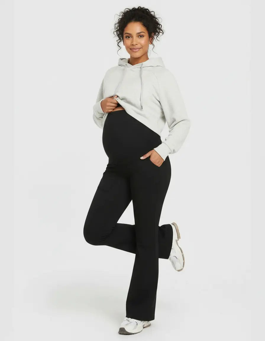 Pregnant woman in black high-waist pocketed flare-leg maternity leggings and a gray hoodie.