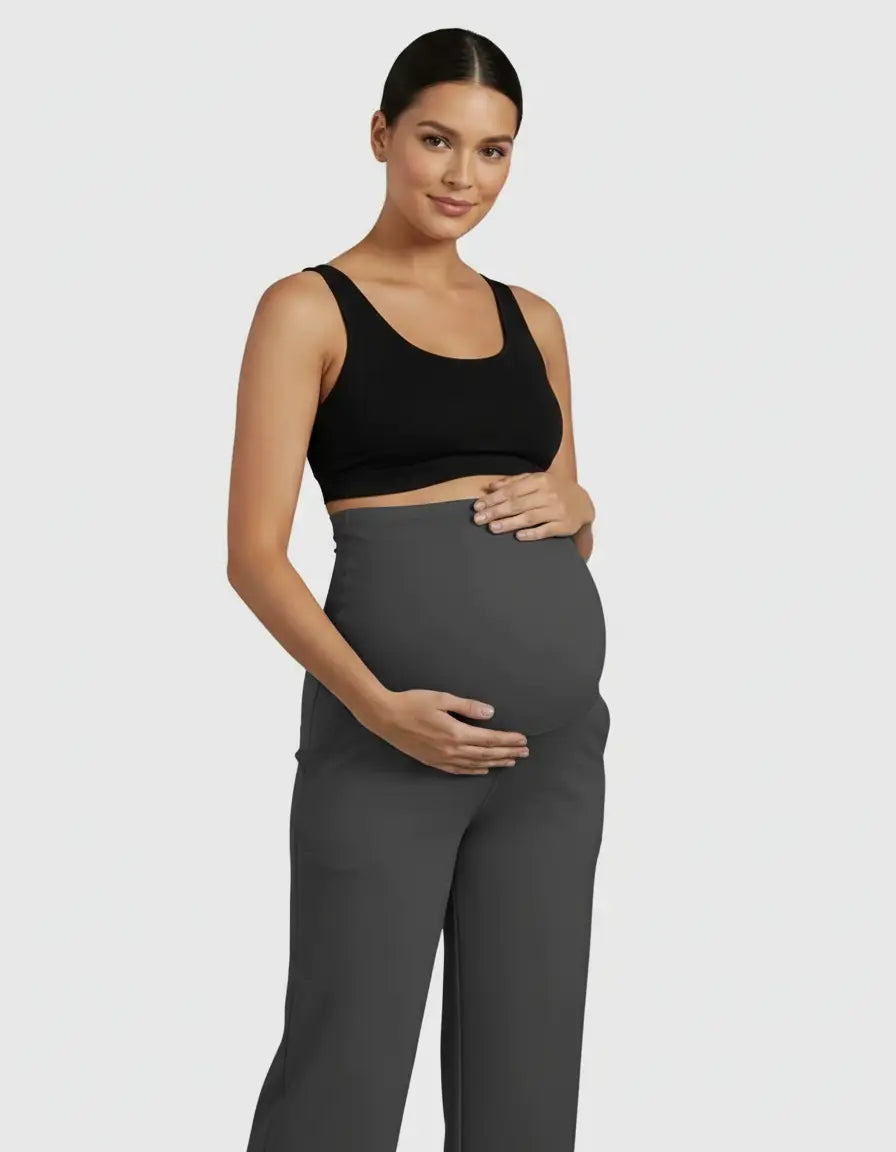 Smiling pregnant woman in a black bra and dark gray high-waist straight-leg maternity pants.