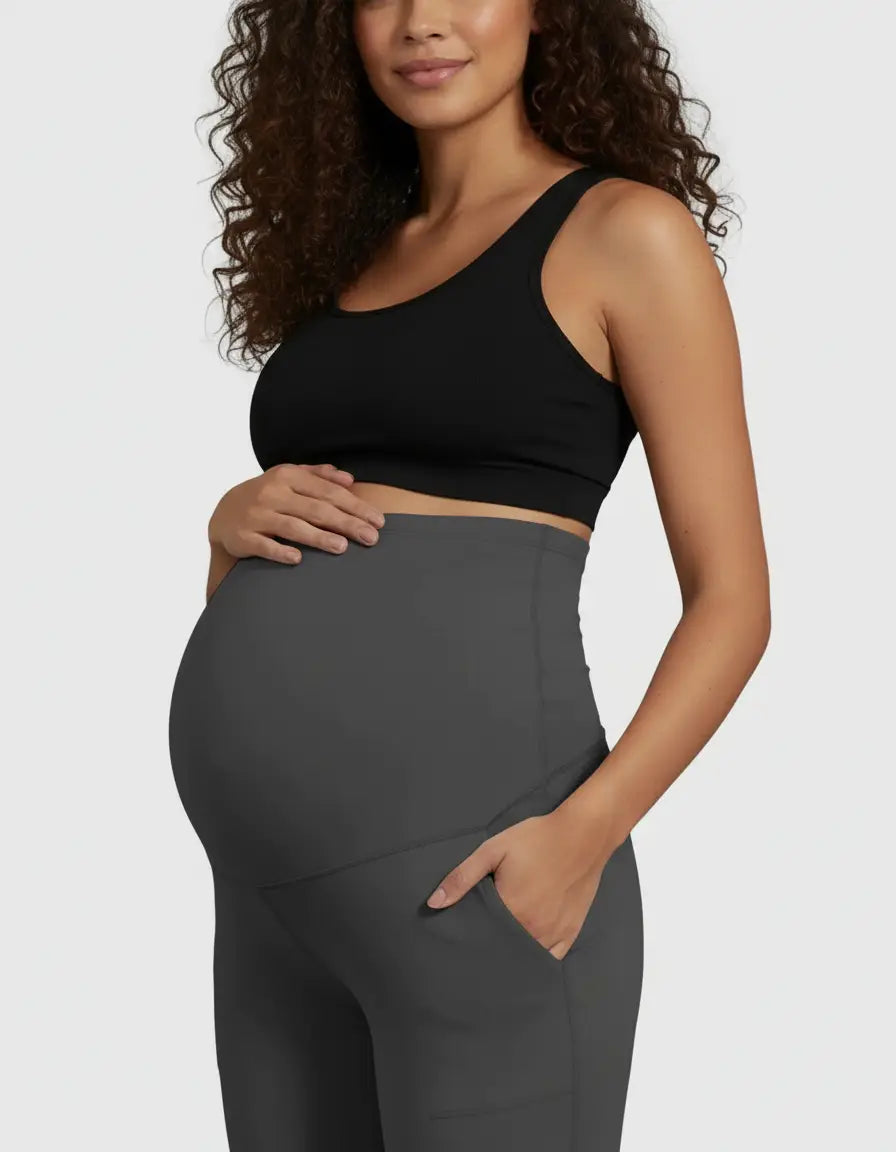 Pregnant woman in dark grey high-waist straight-leg maternity pants with pockets and a black sports bra.