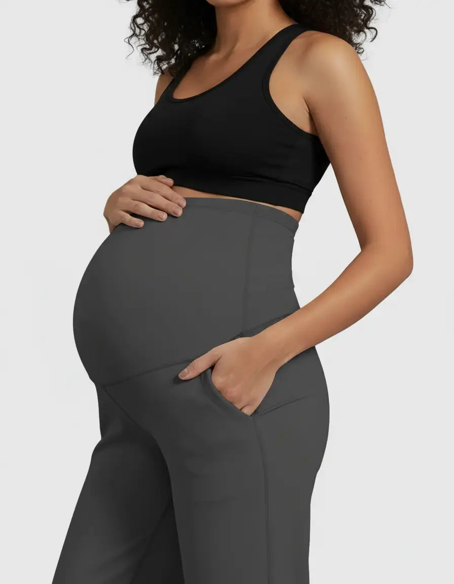 Pregnant woman in dark gray high-waist straight-leg maternity pants with pockets and a black sports bra.