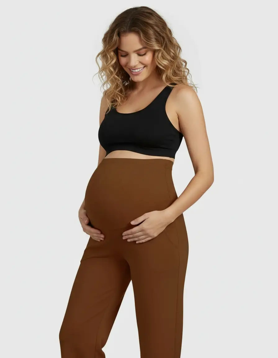 Smiling pregnant woman in brown high-waist straight-leg maternity pants and a black sports bra.