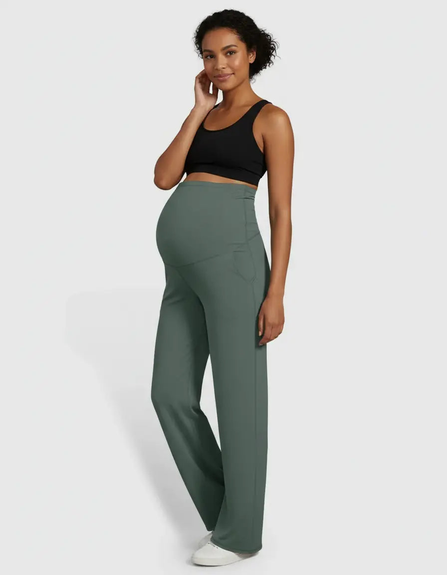 Smiling pregnant woman wearing green high-waist straight-leg maternity pants and a black sports bra.