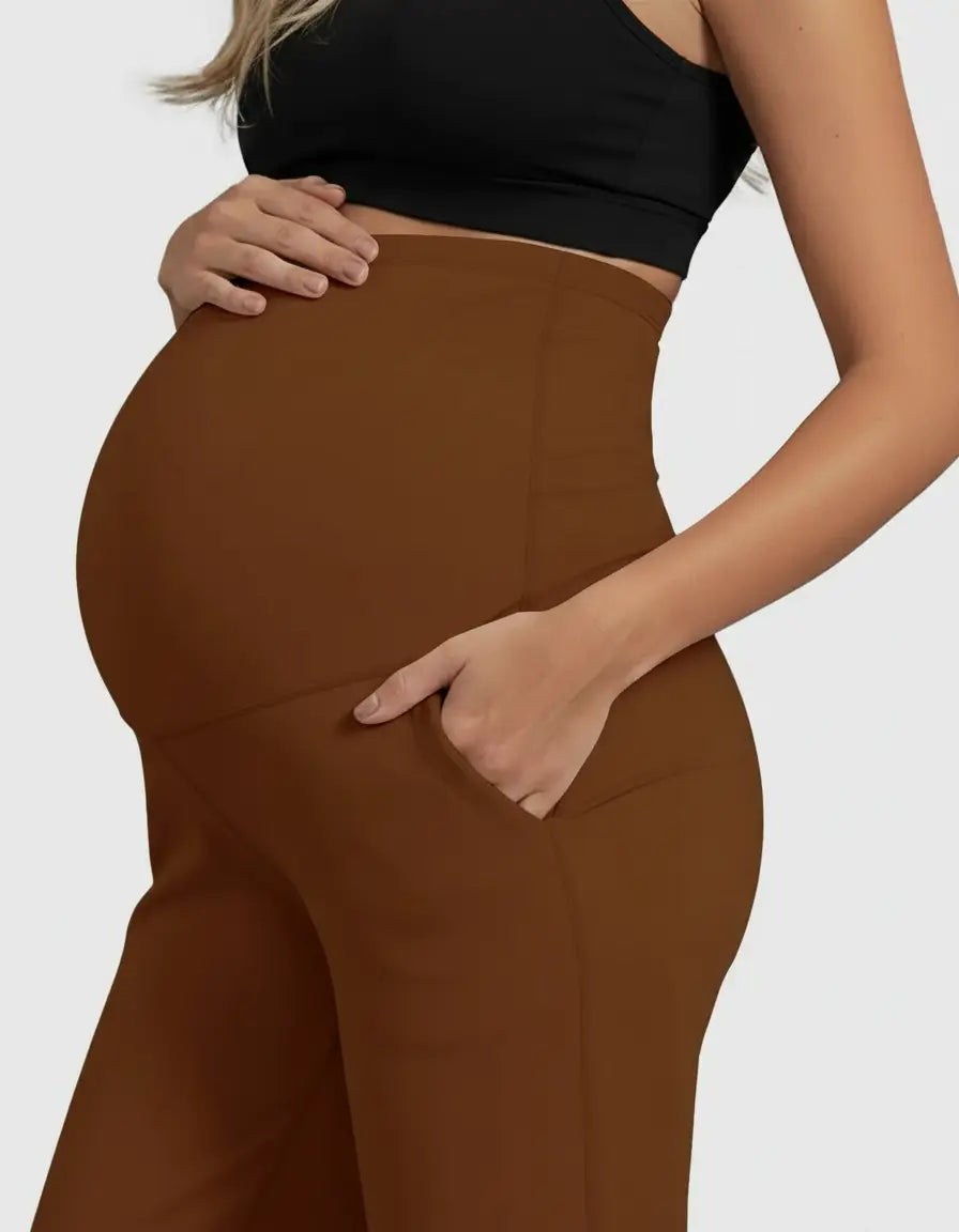 Pregnant woman wearing high-waist, straight-leg brown maternity pants with pockets, supporting her belly.