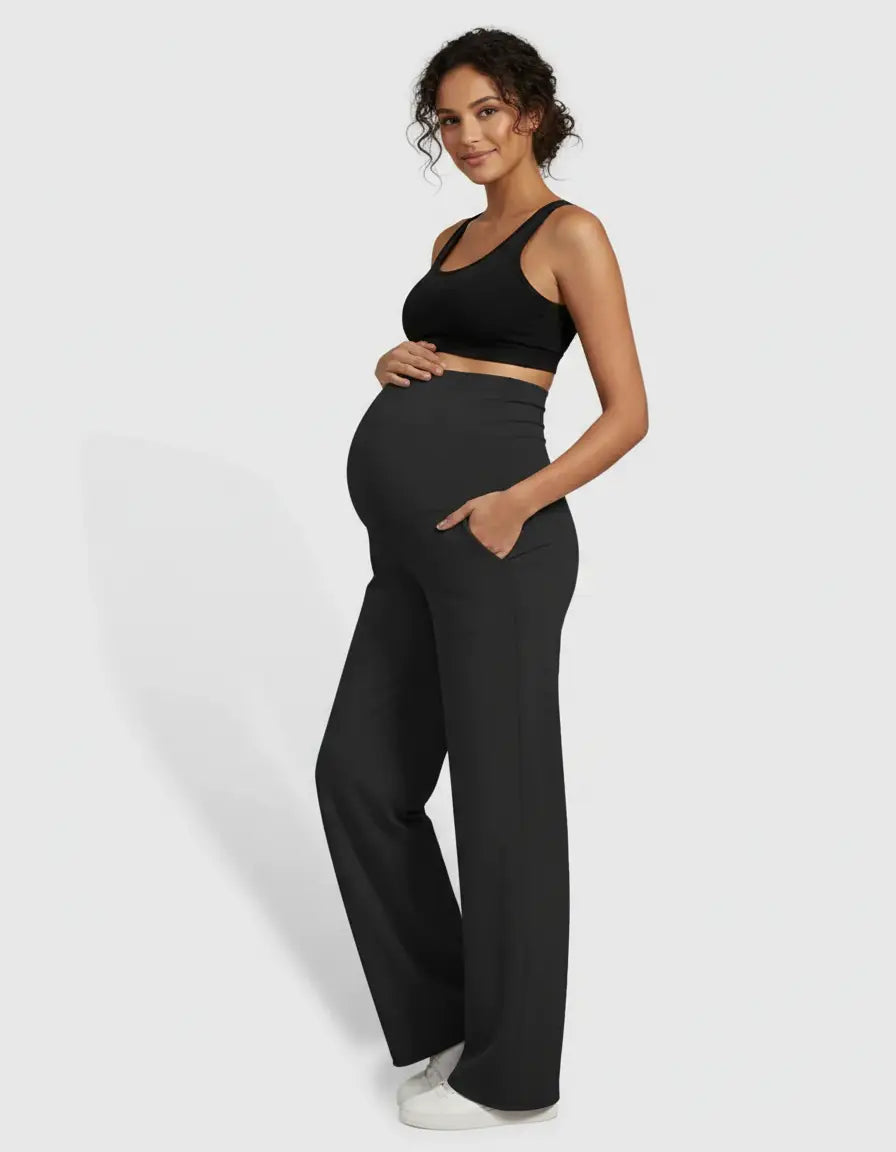 Smiling pregnant woman in black high-waist straight-leg maternity pants with pockets and a black bra.