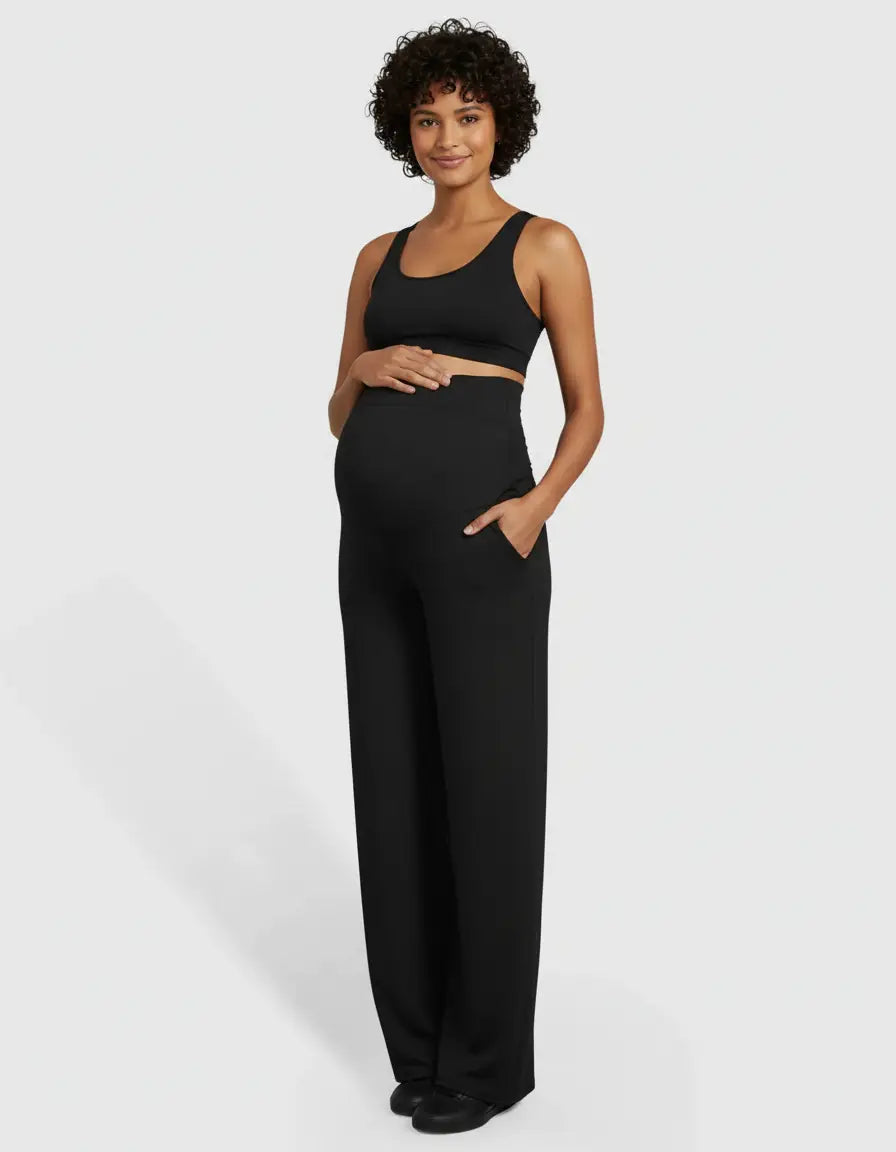 Smiling pregnant woman in black high-waist straight-leg maternity pants with pockets and a matching bra top.