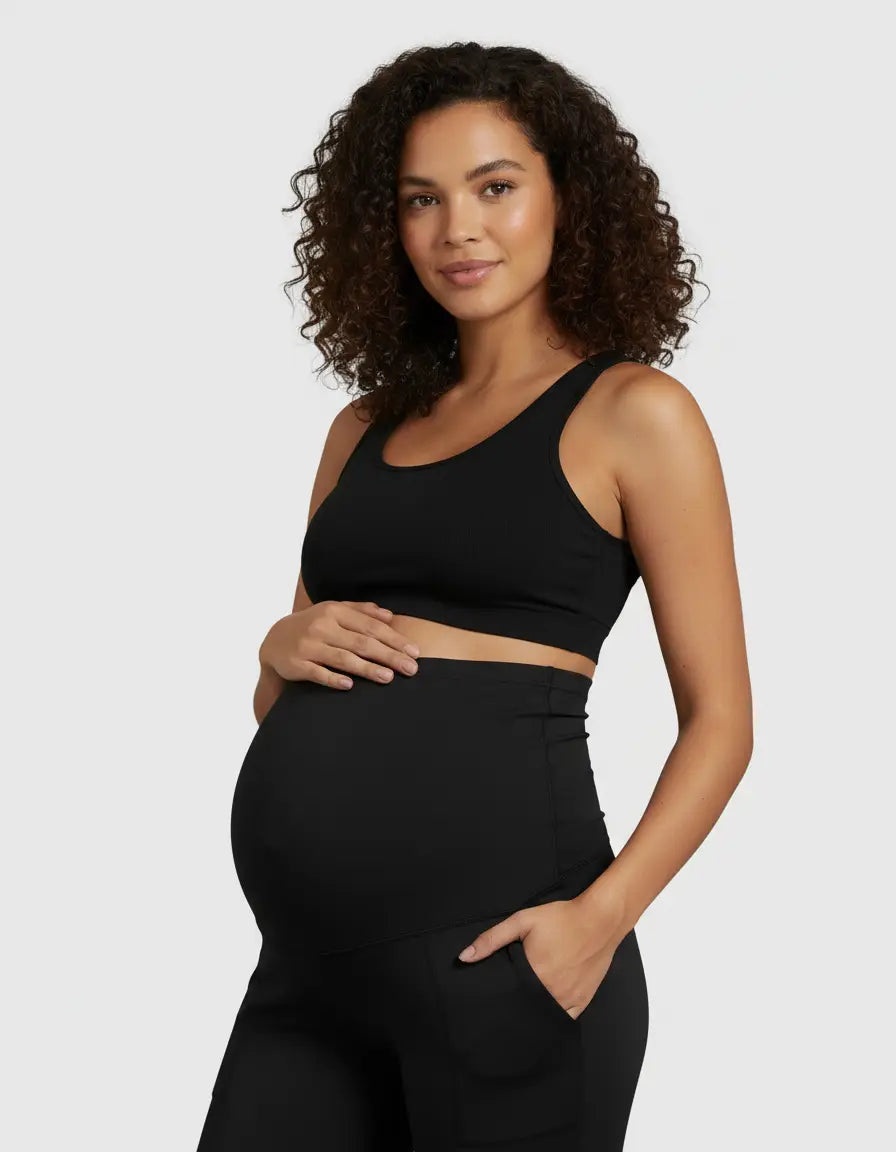 Pregnant woman in black high-waist straight-leg maternity pants and a matching crop top, cradling her bump.