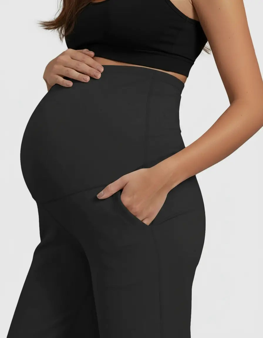 Pregnant woman in black high-waist straight-leg maternity pants with a hand in the pocket.