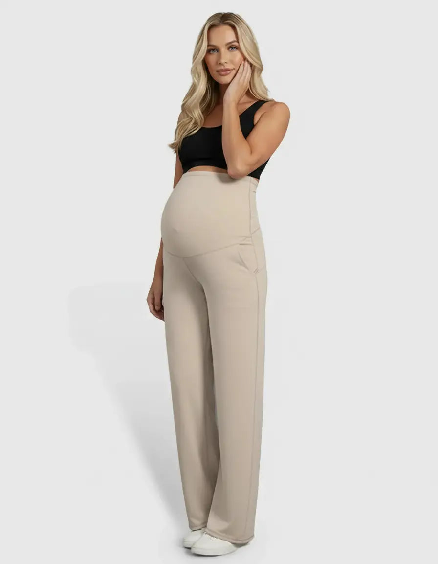 Blonde pregnant woman in a black crop top and high-waist, straight-leg beige maternity pants.