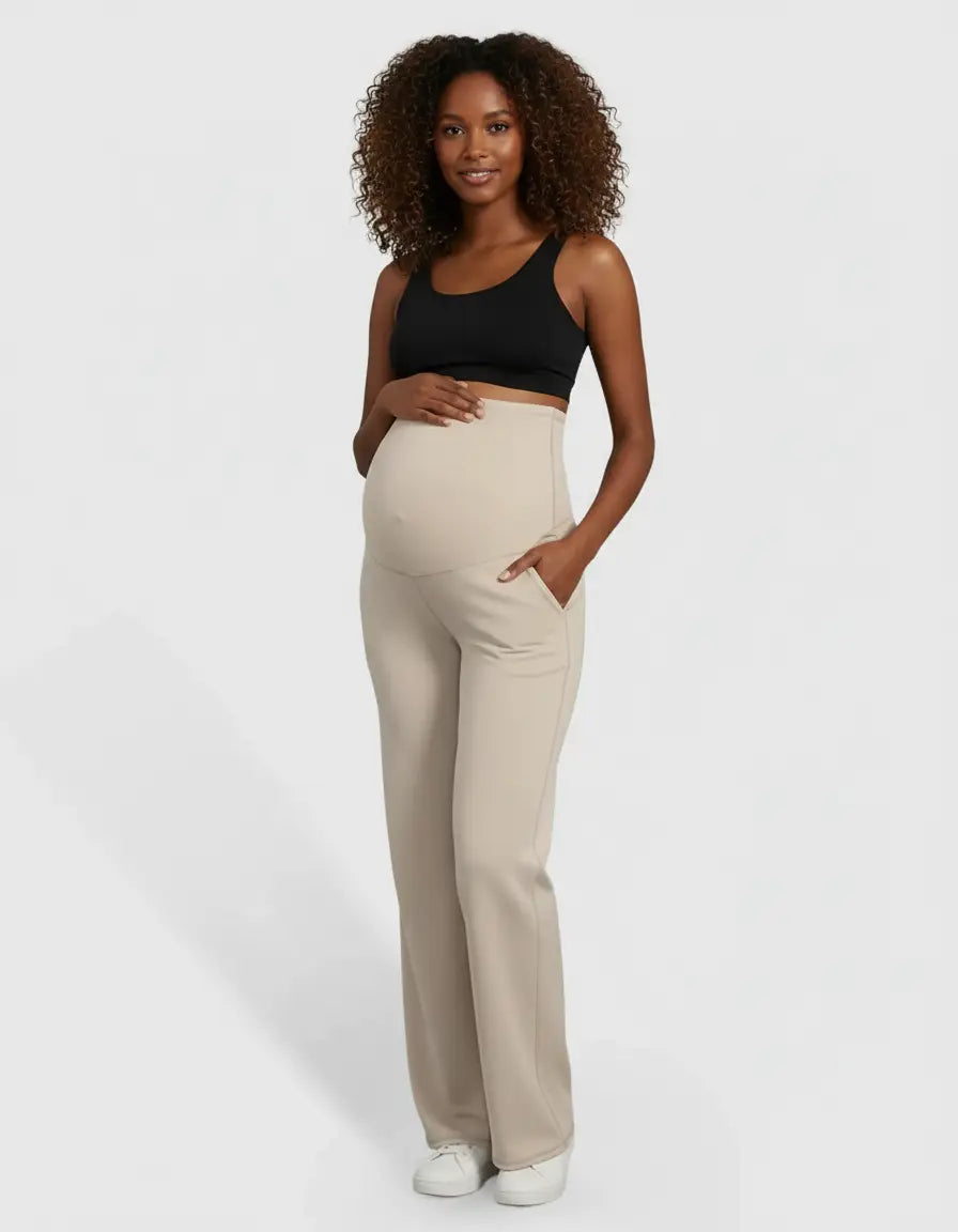 Smiling pregnant woman in beige high-waist straight-leg maternity pants with pockets and a black sports bra.
