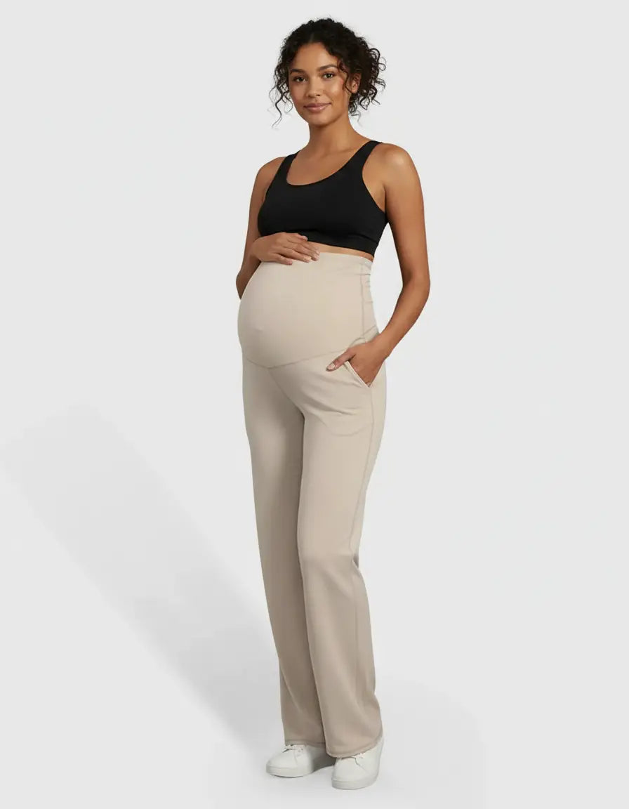 Pregnant woman in high-waist, straight-leg beige maternity pants with pockets and a black sports bra.
