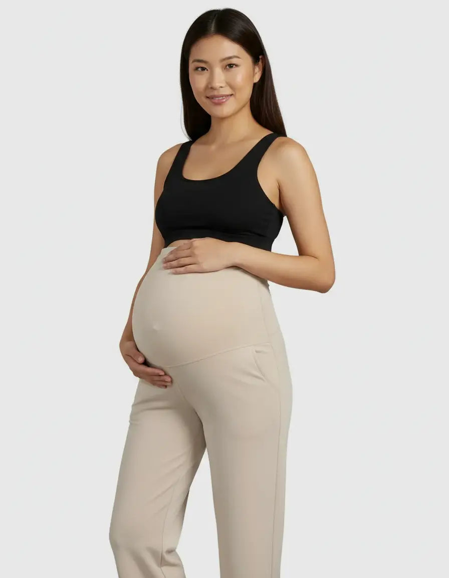 Smiling pregnant woman in a black top and beige high-waist straight-leg maternity pants.