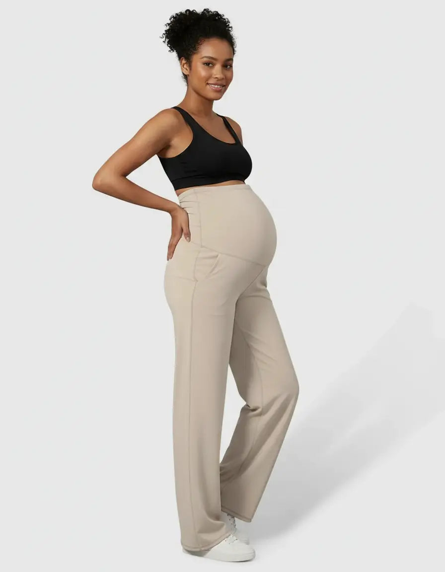 Smiling pregnant woman in beige high-waist straight-leg maternity pants and a black sports bra.