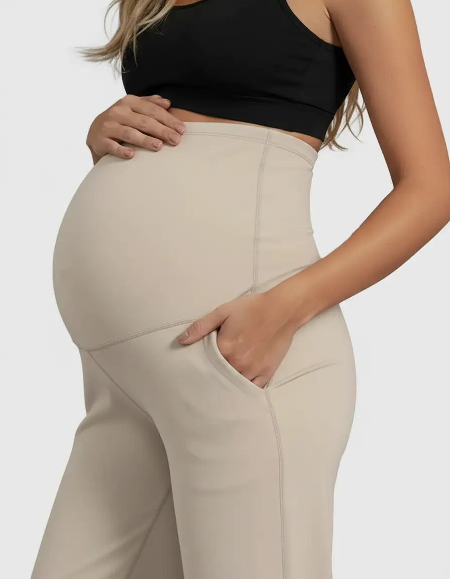 Pregnant woman in beige high-waist straight-leg maternity pants with pockets and a black crop top.