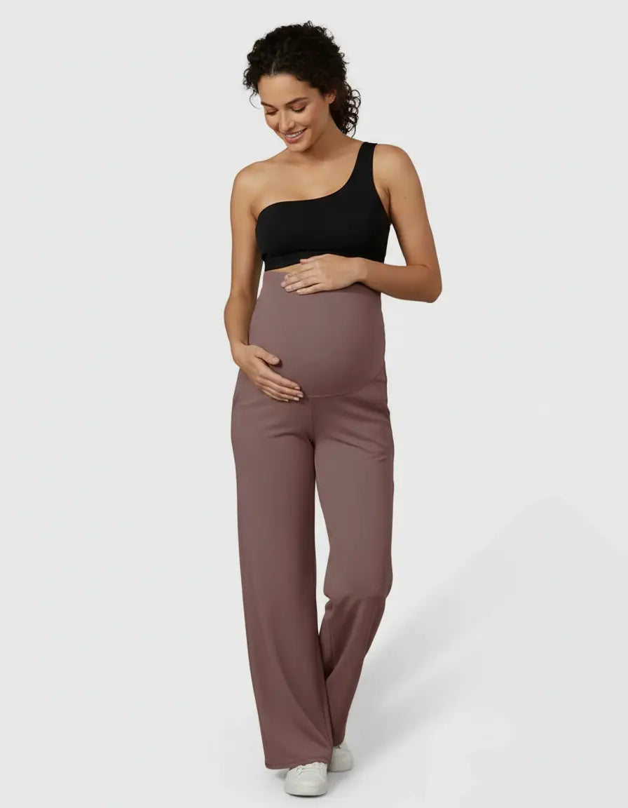 Pregnant woman wearing black one-shoulder top and high-waist straight-leg maternity pants in a soft mauve color.