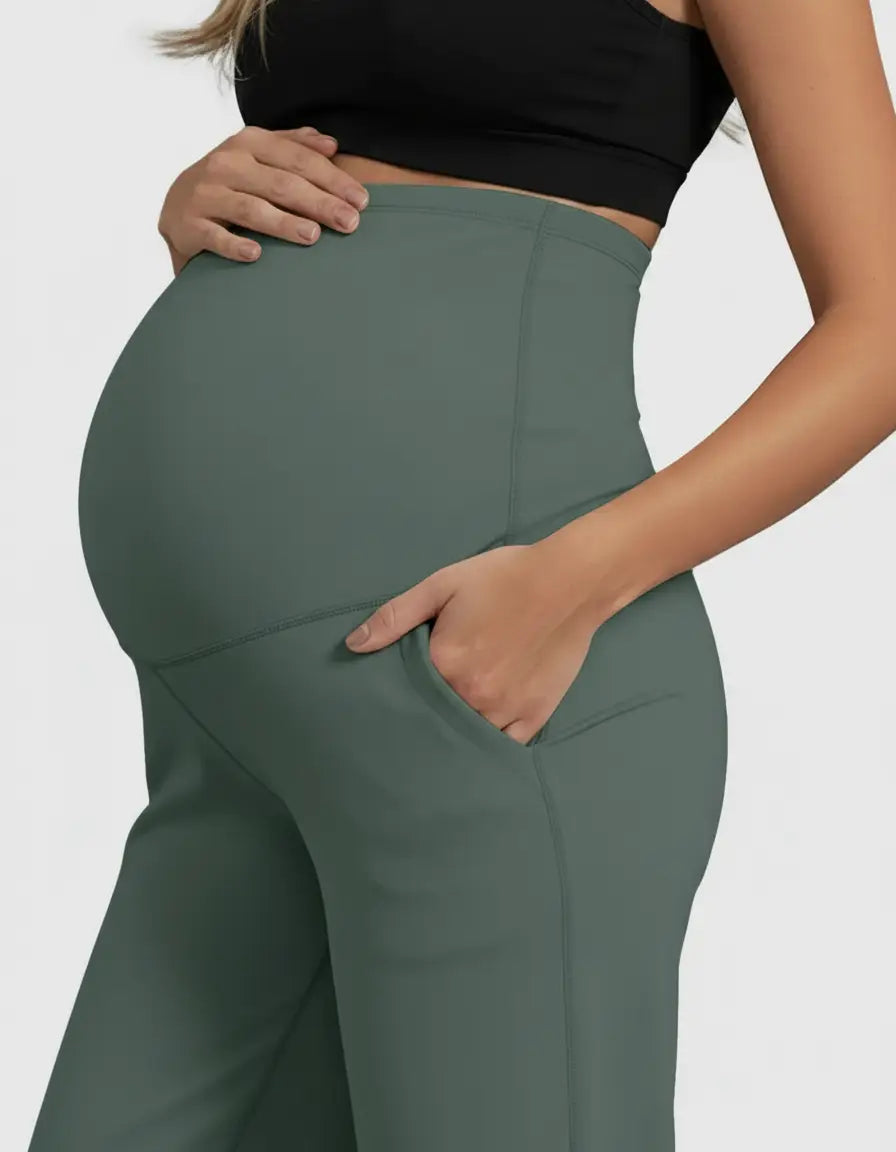Maternity model wearing high-waist, straight-leg, dark green maternity pants with pockets.