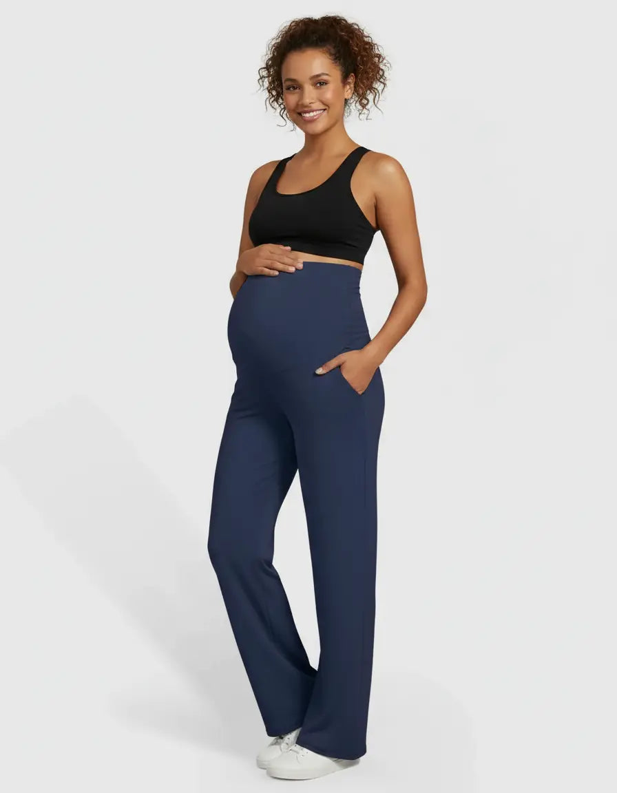 Smiling pregnant woman in navy high-waist straight-leg maternity pants with pockets and a black sports bra.