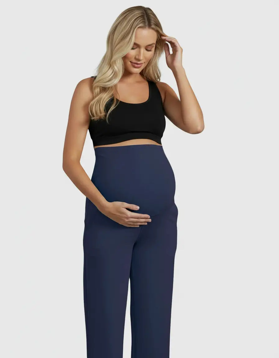 Blonde pregnant woman wearing navy high-waist straight-leg maternity pants and a black sports bra.