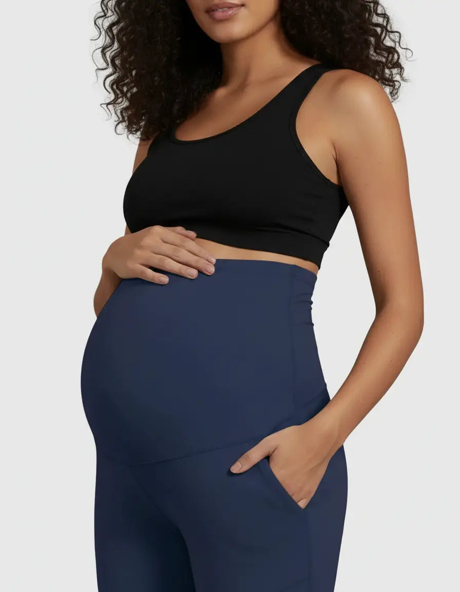 Pregnant woman in black top and navy high-waist straight-leg maternity pants with a hand in the pocket.