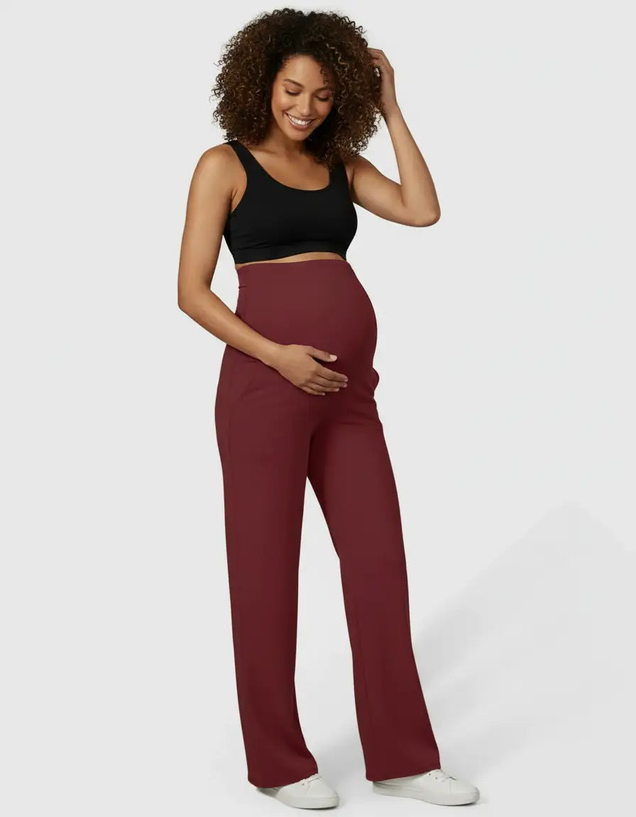 Smiling pregnant woman in a black bra and comfortable high-waist straight-leg burgundy maternity pants.