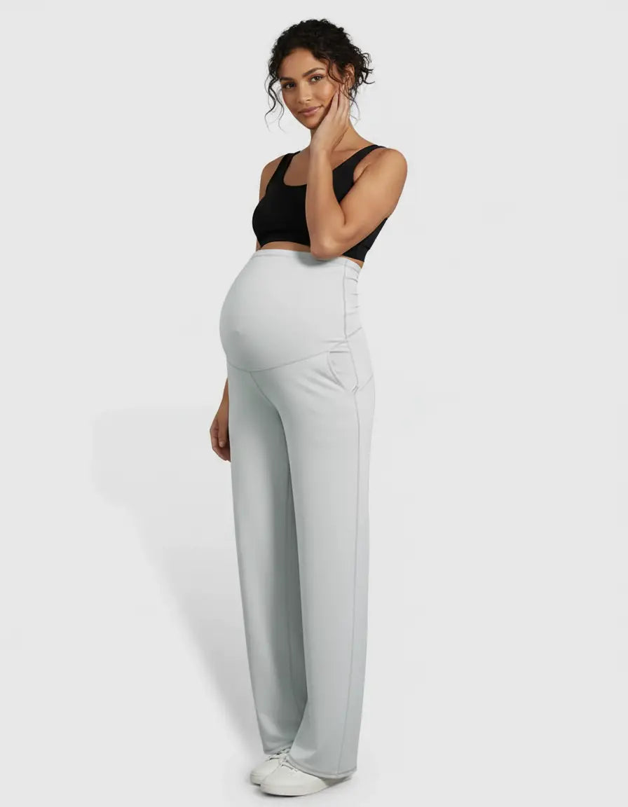 Pregnant woman in light grey high-waist straight-leg maternity pants and a black crop top.