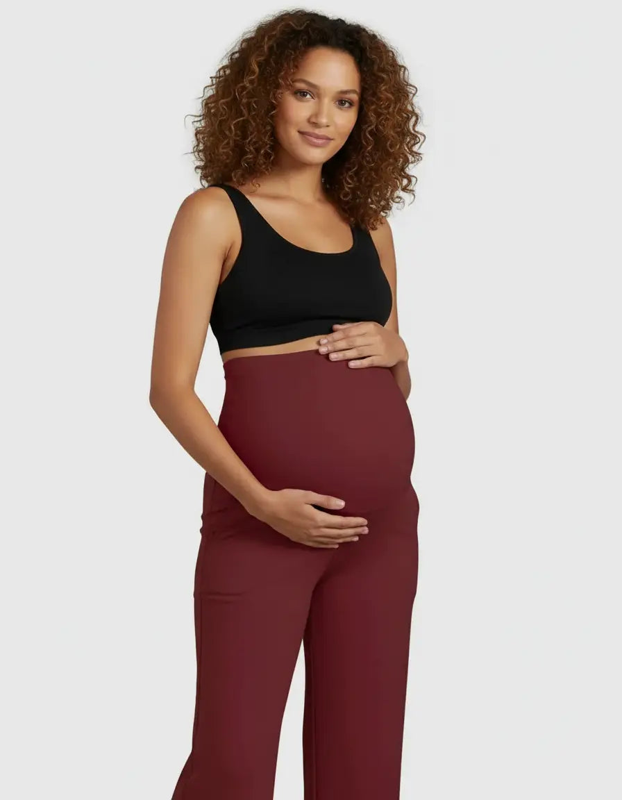 Smiling pregnant woman in a black crop top and comfortable high-waist straight-leg maternity pants in a deep red color.