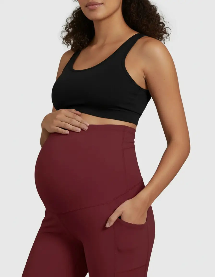 Pregnant woman wearing a black sports bra and high-waist, straight-leg, burgundy maternity pants with pockets.