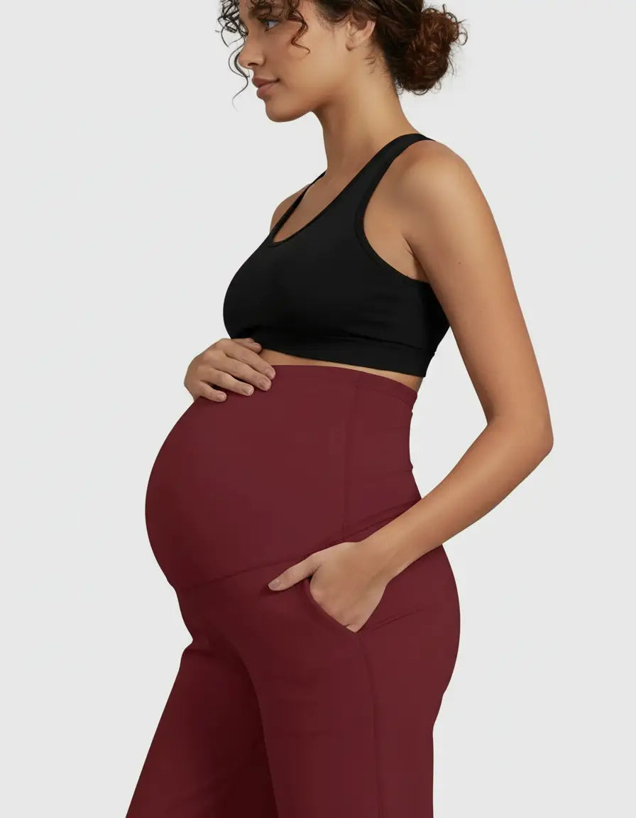 Pregnant woman wearing high-waist, straight-leg burgundy maternity pants with pockets and a black sports bra.