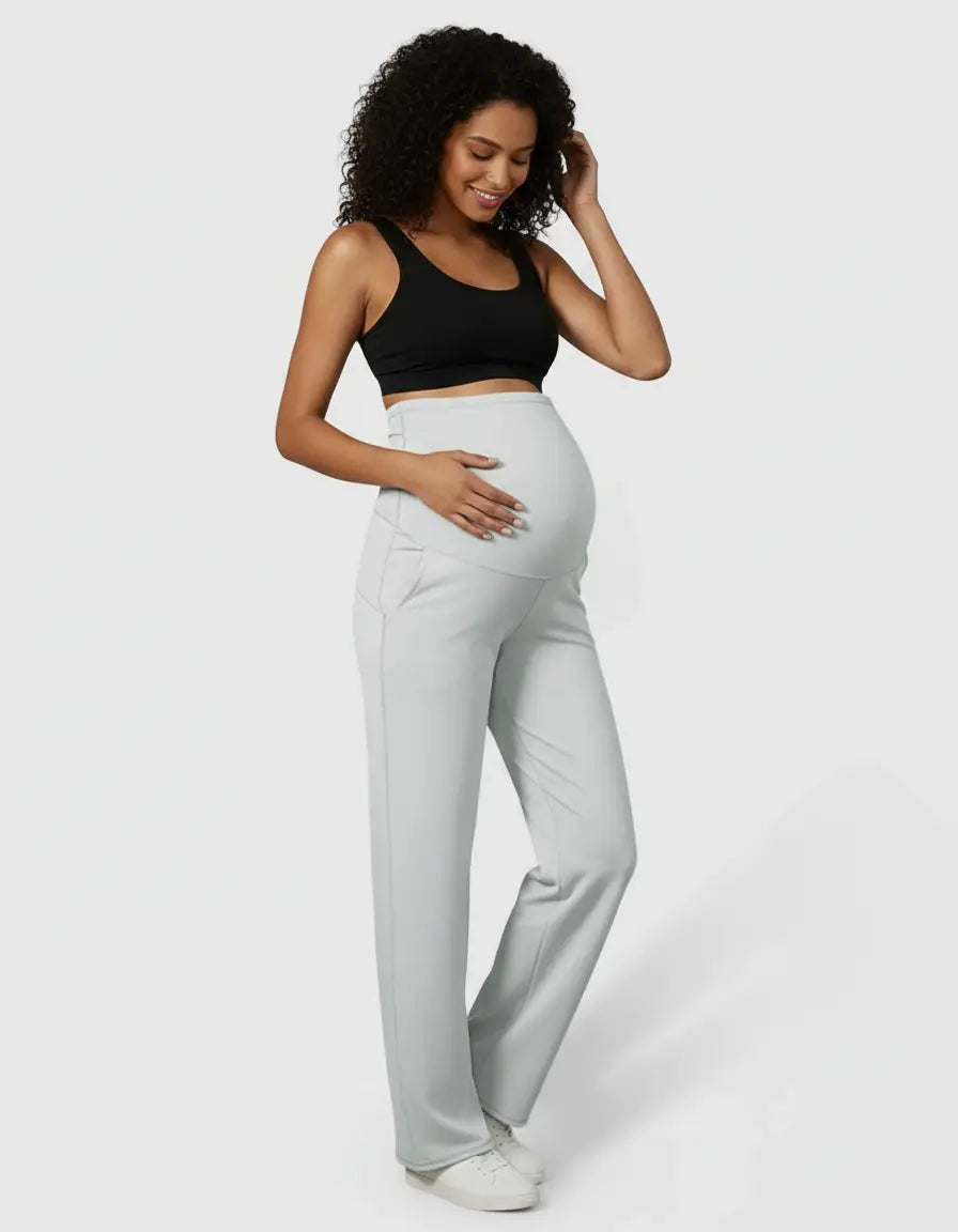Smiling pregnant woman in light grey high-waist straight-leg maternity pants and a black bra.
