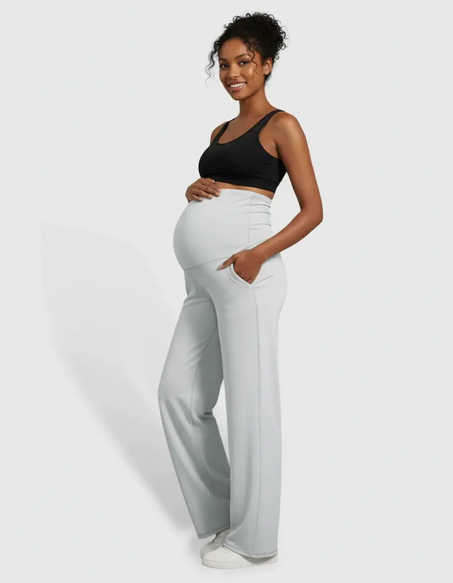 Smiling pregnant woman in light grey high-waist straight-leg maternity pants with pockets and a black bra.