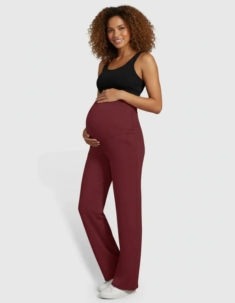 Smiling pregnant woman in high-waist, straight-leg burgundy maternity pants and a black tank top.