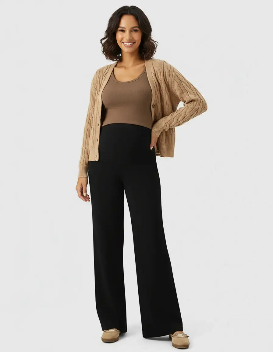 Smiling pregnant woman in black high-waist wide-leg maternity wool pants, brown tank, and cardigan.