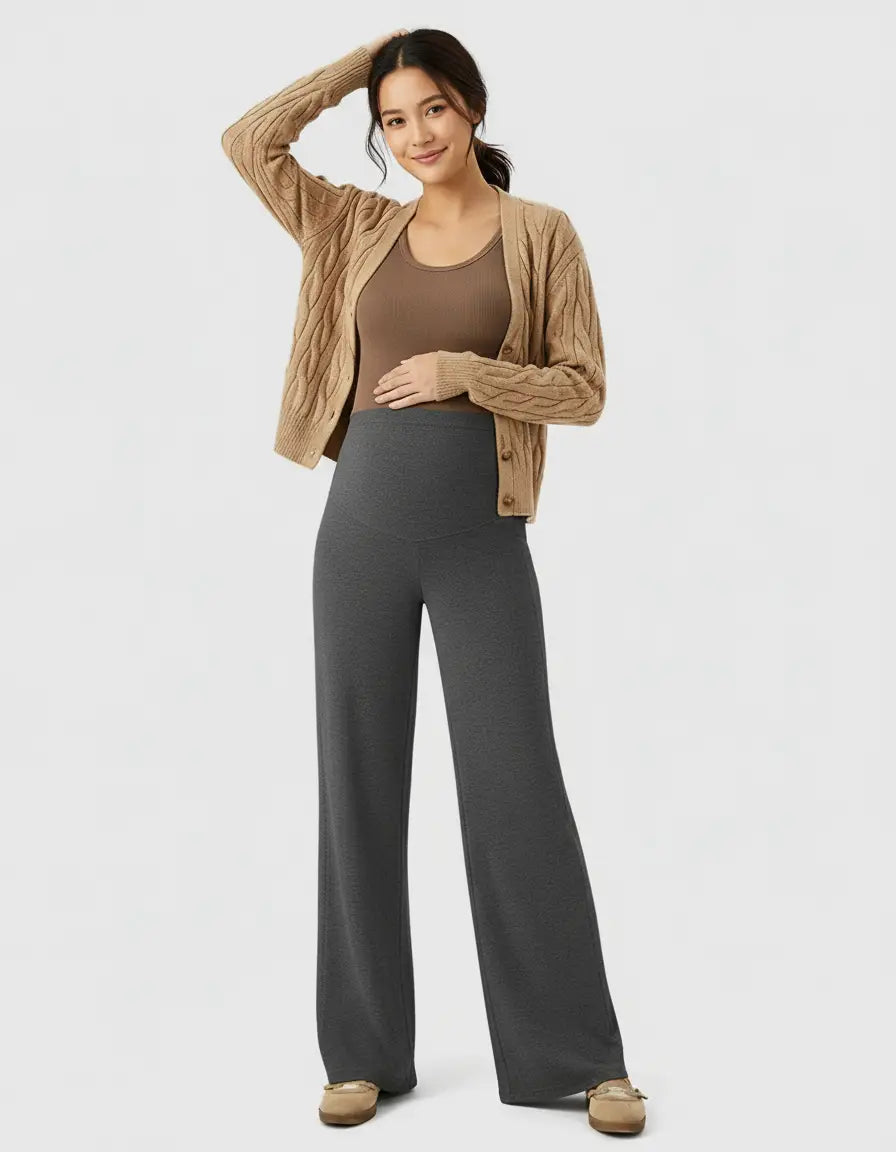 Smiling pregnant woman in charcoal high-waist wide-leg maternity wool pants, brown tank, and cardigan.