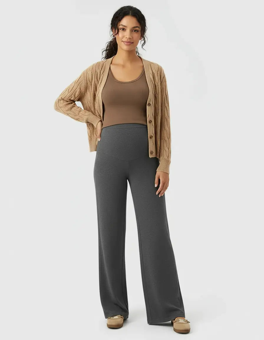 Smiling pregnant woman in charcoal high-waist wide-leg maternity wool pants, brown tank, and cardigan.