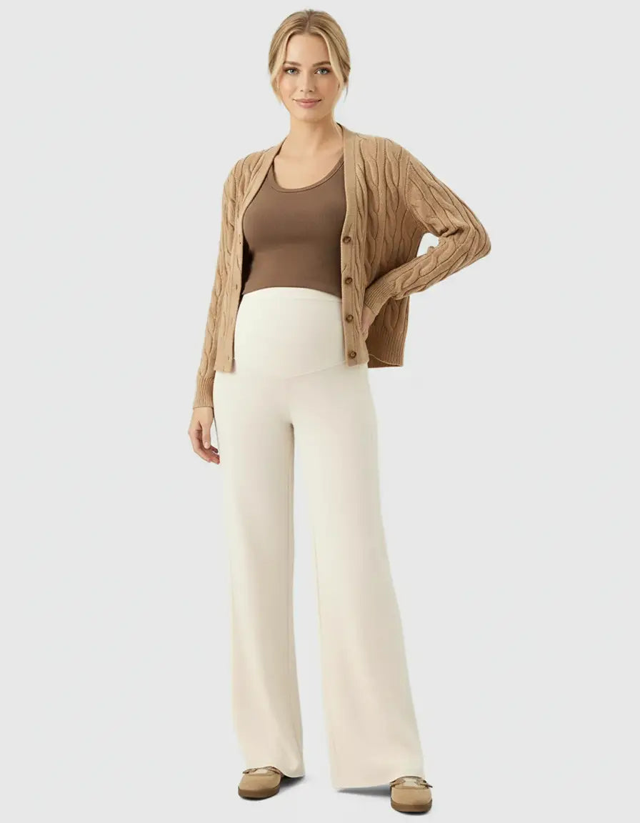 Woman in cream high-waist wide-leg maternity wool pants, brown tank top, and cable-knit cardigan.